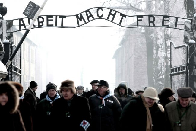 Byli więźniowie obozu koncentracyjnego z bliskimi przechodzą przez bramę KL Auschwitz (PAP/Grzegorz Momot)